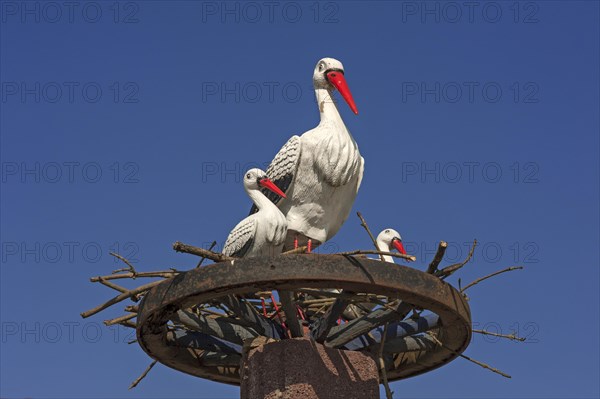 Stork figures on a wagon wheel against blue sky