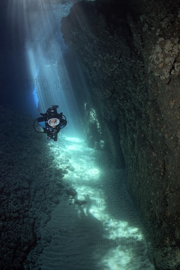 Diver in a narrow crevice with sun rays beaming down