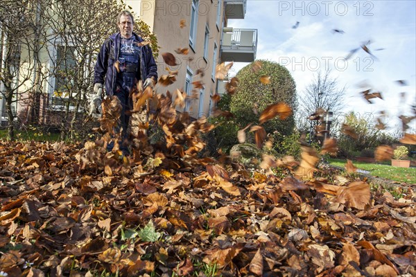 Janitor with leaf blower blowing up leaves in a residential area