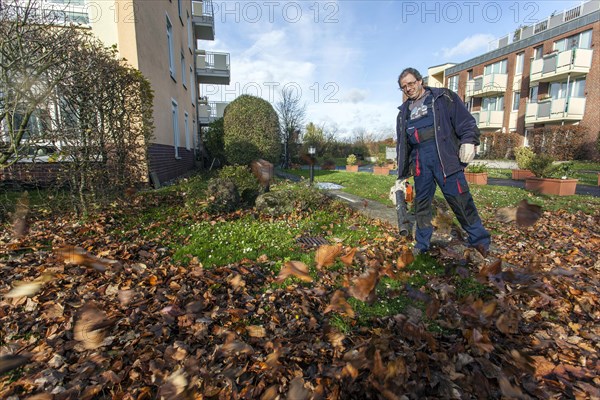 Janitor with leaf blower blowing up leaves in a residential area