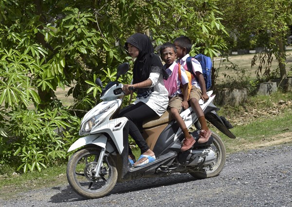Woman wearing a headscarf with two school children on a scooter