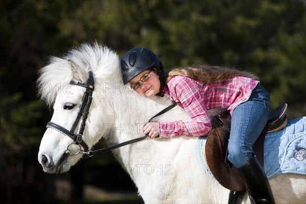 Happy girl sitting on a pony and cuddling