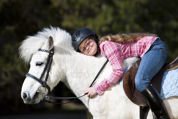 Happy girl sitting on a pony and cuddling