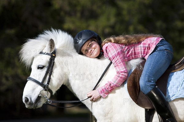 Happy girl sitting on a pony and cuddling