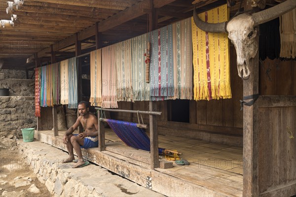 Ngada man sitting on porch with Ikat fabrics and buffalo horn