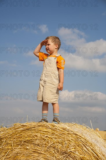 Little boy being on the lookut out on a straw bale