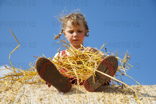 Little girl sitting on a straw bale under a cloudy blue sky