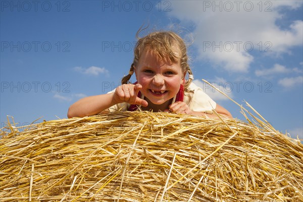 Little girl lying on a straw bale under a cloudy blue sky