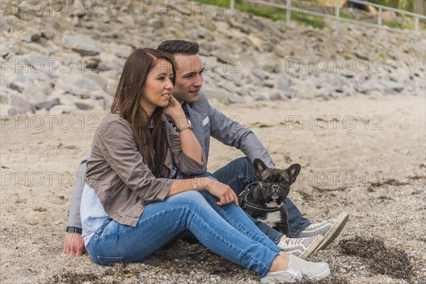 Couple and a French Bulldog sitting on the beach