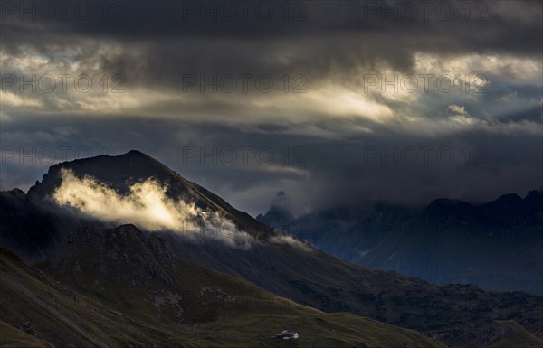 Clouds with sunny spot in front of dark mountain peaks