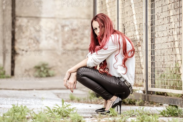 Young woman with long red hair sitting in front of a chain link fence