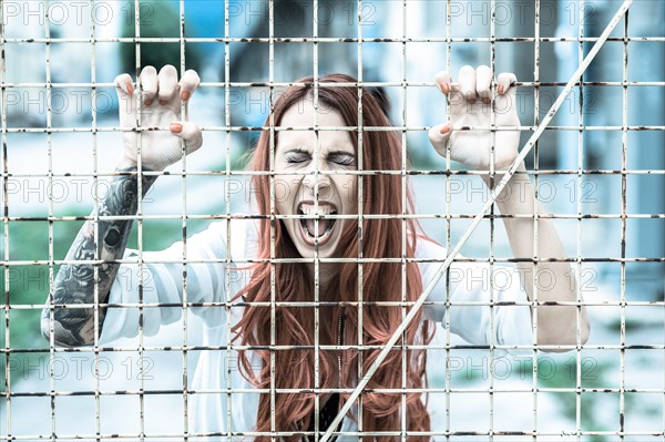 Young woman with long red hair and a tattoo screaming behind bars