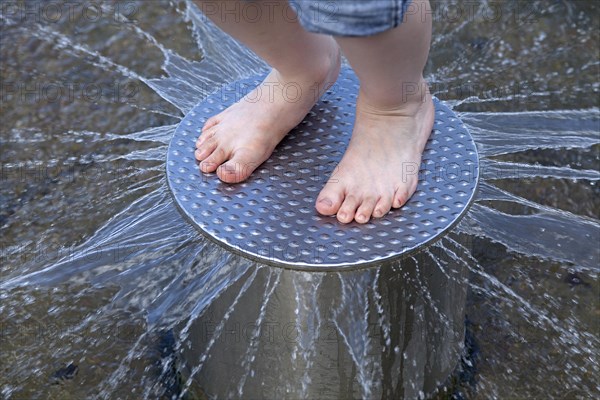 Child's feet on a metal plate with water squirting out