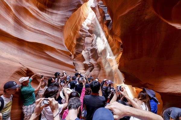 Tourists gather around a sunbeam filtering through rocks into the canyon