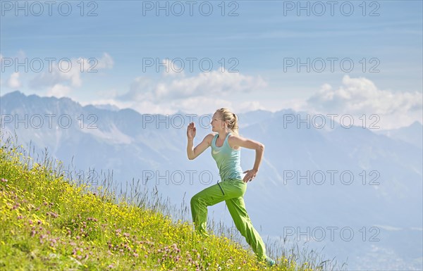 Young woman in her twenties running up field in mountains