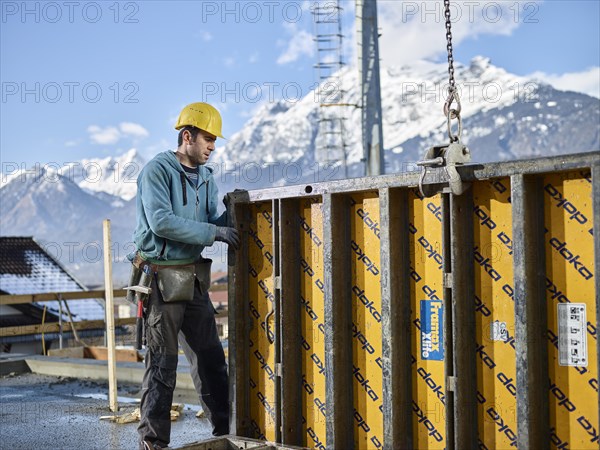 Construction worker lifting shuttering wall with crane