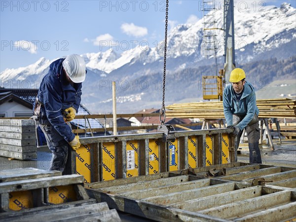 Construction workers lifting shuttering wall with crane