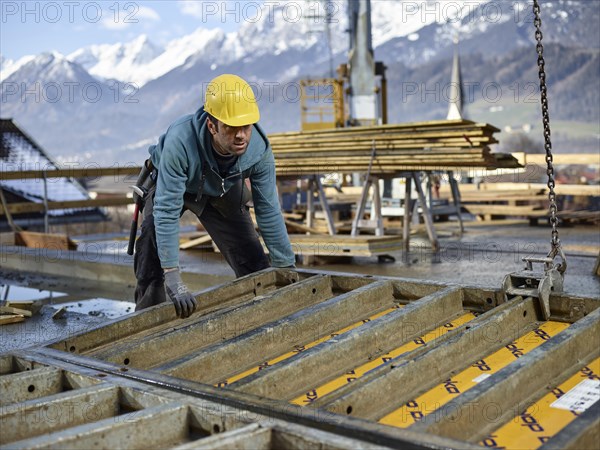 Construction worker lifting shuttering wall with crane