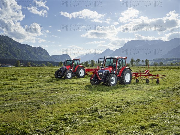 Two tractors mowing and tedding the cut hay