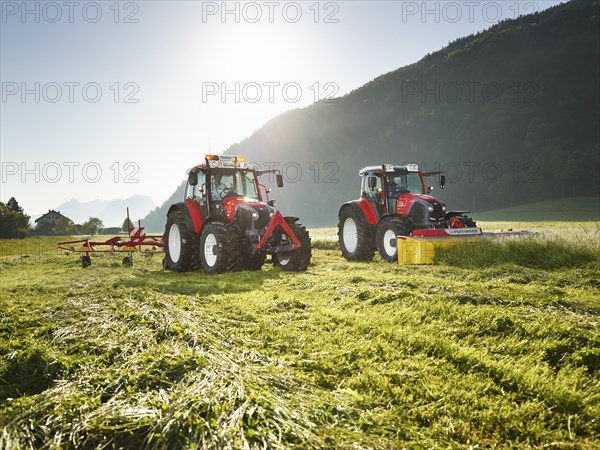 Two tractors mowing and tedding the cut hay