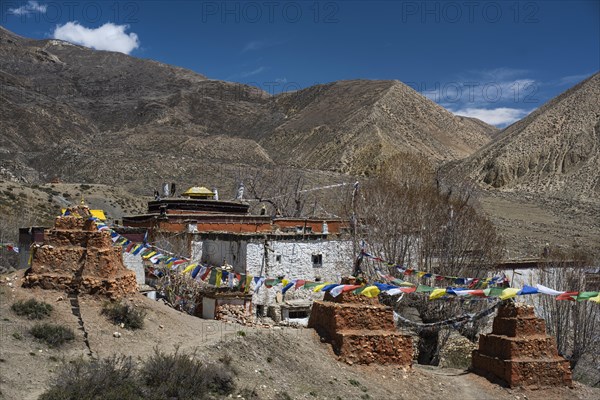 Ghar Gompa of Lo Gekar with prayer flags in front of mountain landscape