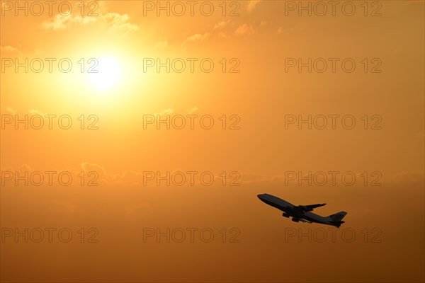 Airplane taking off silhouetted against a sunset