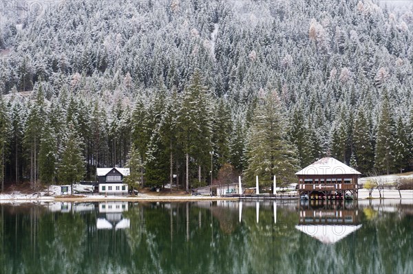 Snow-covered forest and houses reflected in Lake Toblach