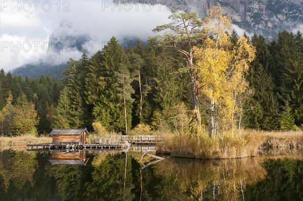 Hut and trees in autumn reflected in the Volser Weiher lake