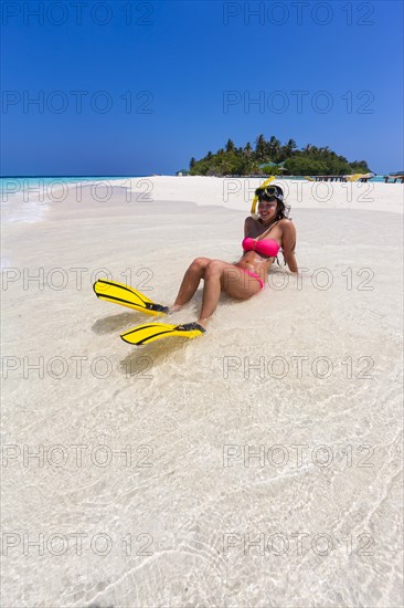 Woman with flippers and diving goggles sitting on a sand bank