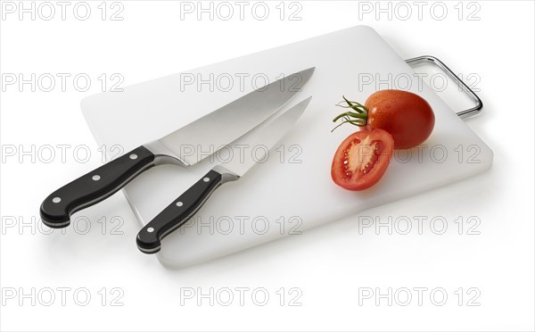 Two knives on a white cutting board with tomatoes