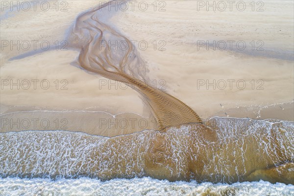 Creek with reddish ferruginous water flows over a sandy beach into the sea