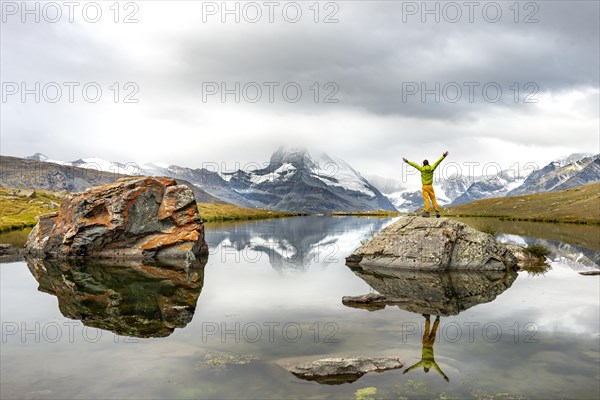 Hiker stands on rocks in the lake and stretches his arms into the air