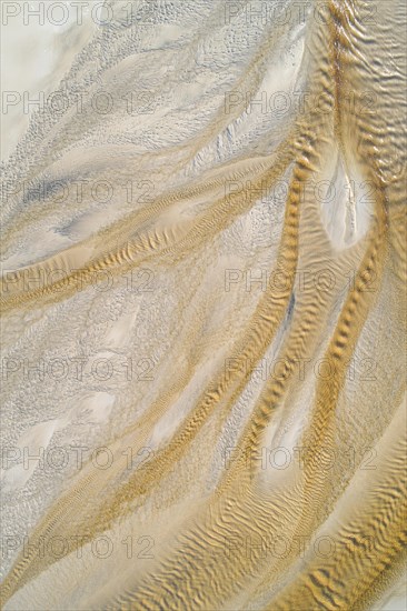 Creek with reddish ferruginous water flows over a sandy beach into the sea