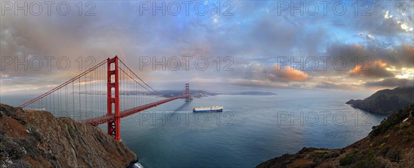 Panoramic view of the Golden Gate Bridge at sunset with a rainbow and storm clouds