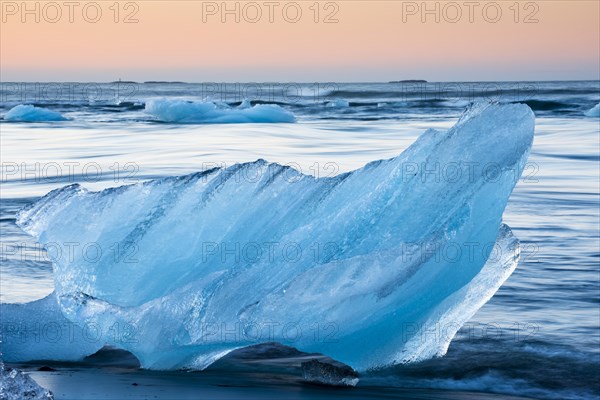 Block of ice on a black beach being lapped by the sea