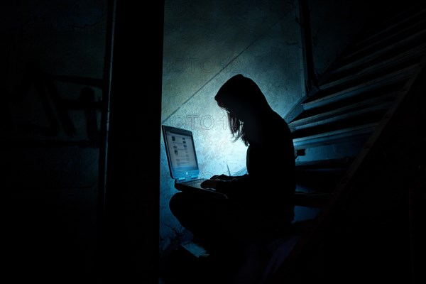 Female computer hacker sitting with a laptop in the dark