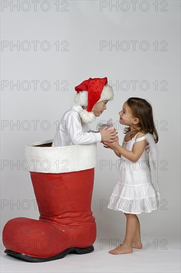 Boy in a Christmas boot handing a small Christmas present to a girl dressed as an angel