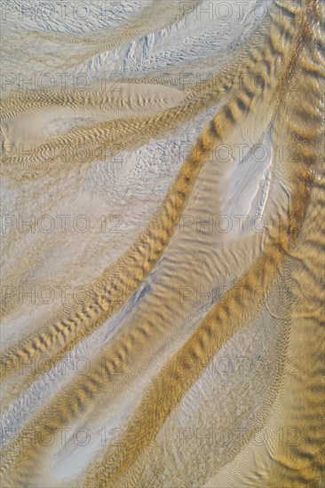 Creek with reddish ferruginous water flows over a sandy beach into the sea