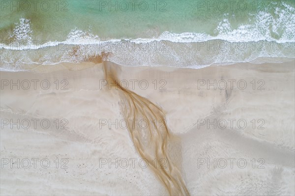 Creek with reddish ferruginous water flows over a sandy beach into the sea
