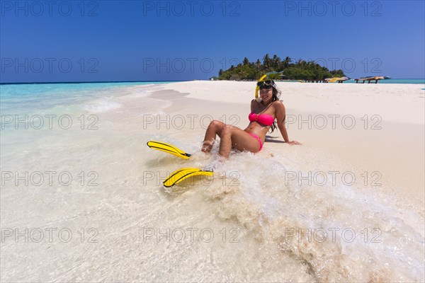 Woman with flippers and diving goggles sitting on a sand bank