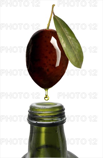 Olive oil dripping from an olive into a bottle