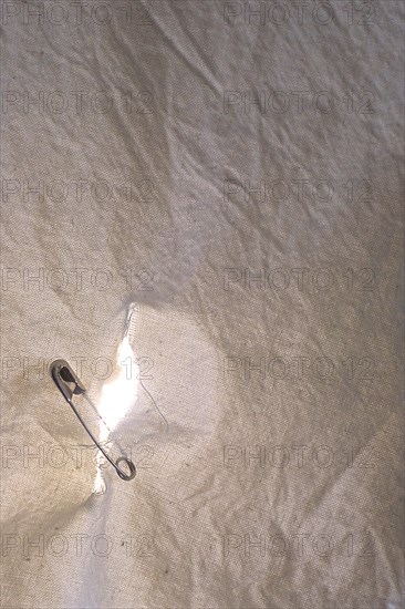 Hole in a sheet being held together by a safety pin