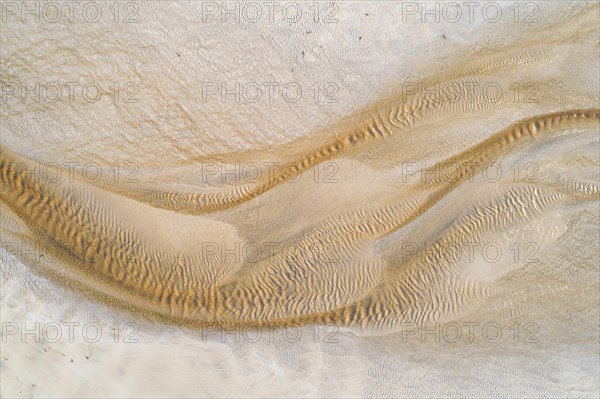 Creek with reddish ferruginous water flows over a sandy beach into the sea