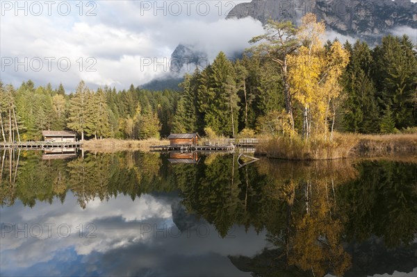 Hut and trees in autumn reflected in the Volser Weiher lake