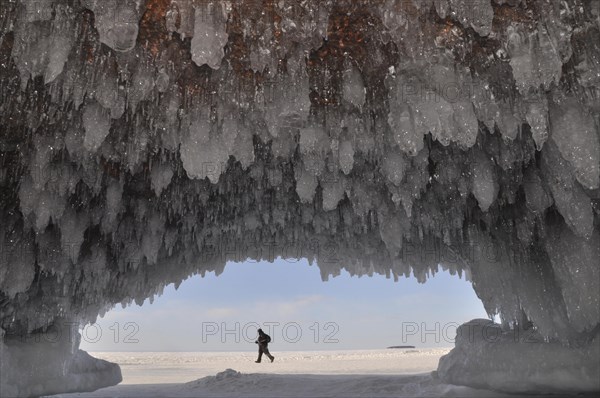 Ice formations and icicles hanging from ceiling in a cave and a man walking on frozen Lake Superior