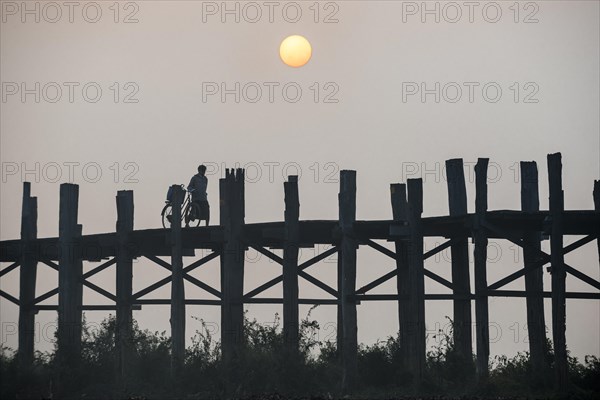 Man with a bicycle on a teak bridge