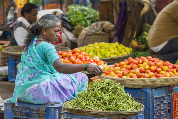 A woman is selling chilis and tomatoes at the weekly vegetable market