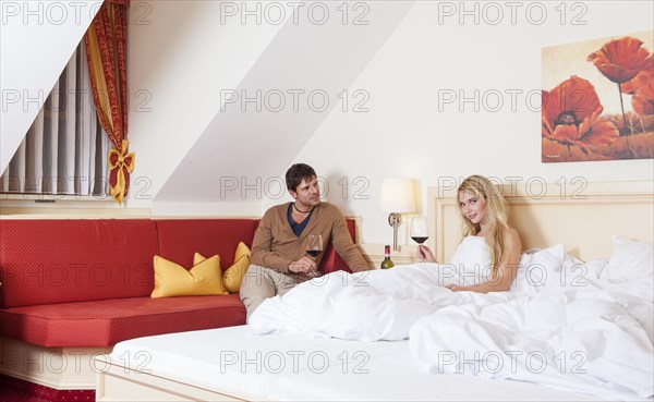 Man and woman with a glass of red wine in a bedroom of a hotel