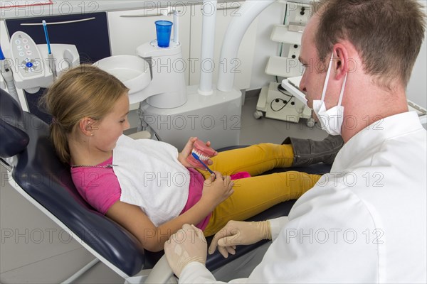 Dentist showing a girl the proper use of a toothbrush