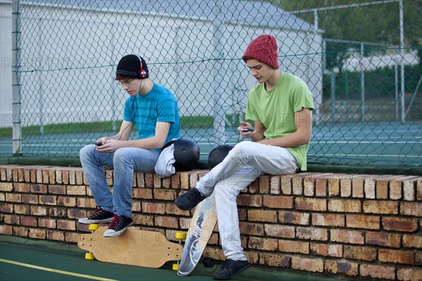 Two teenage boys sitting on a brick wall